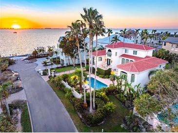 Breathtaking aerial view of a luxurious waterfront home with a pool and tropical landscaping at sunset at 1023 Tocobaga Ln, Sarasota, FL 34236