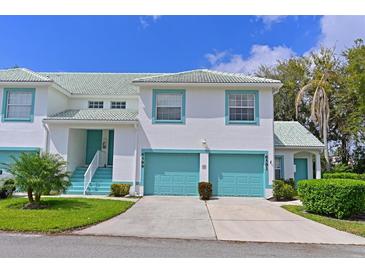 Bright two-story townhome with a two-car garage and turquoise accents, landscaped with green grass, shrubbery, and small trees at 6589 Fairway Gardens Dr # 202, Bradenton, FL 34203