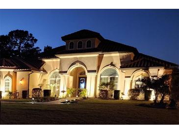 Stunning front exterior of home with a tile roof, arched entrance, and manicured landscaping illuminated at dusk at 9709 Wilderness Trl, Weeki Wachee, FL 34613