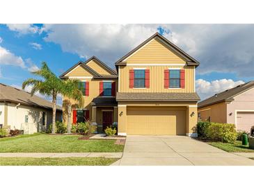 Charming two-story home with a lush green lawn, a palm tree, and red shutters on the windows at 14318 Fissore Blvd, Wimauma, FL 33598