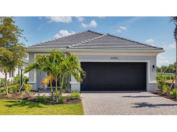 Charming home featuring a well-manicured lawn, paved driveway and a black garage door surrounded by beautiful landscaping at 26936 Lark Ct, Punta Gorda, FL 33955