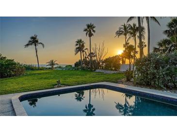 Beautiful backyard featuring a pool, lush lawn, and stunning sunset views over palm trees and the ocean at 4473 Gulf Of Mexico Dr, Longboat Key, FL 34228