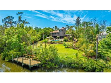Lush backyard featuring a dock, large lawn, mature trees, and a large in-ground pool surrounded by greenery at 5135 Riverwood Ave, Sarasota, FL 34231