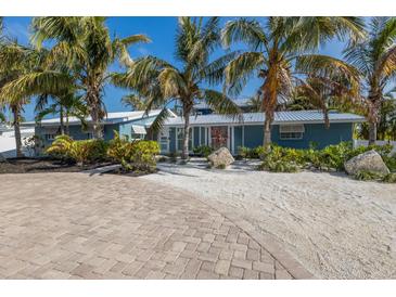 Charming blue home with lush tropical landscaping and circular brick paver driveway at 6201 Holmes Blvd, Holmes Beach, FL 34217