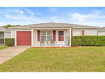 Charming single-story home with a red garage door, tidy landscaping, and a cozy front porch seating area at 29353 Princeville Dr, San Antonio, FL 33576