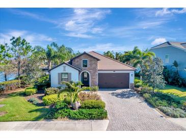 Beautiful single-story home with stone accents, a tile roof, and a paver driveway surrounded by lush landscaping at 12026 Perennial Pl, Bradenton, FL 34211