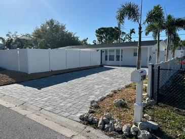 Charming home featuring a brick driveway, white fence, and lush palm trees under a clear blue sky at 2180 Orchid St, Sarasota, FL 34239