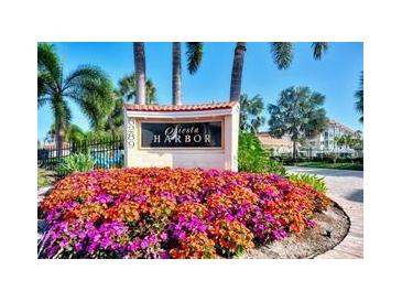 Fiesta Harbor entrance sign with colorful flowers, tropical foliage, and palm trees under a sunny blue sky at 1250 N Portofino Dr # 408Mar, Sarasota, FL 34242