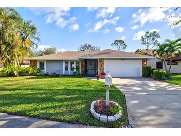 Charming single-story home featuring a manicured lawn and a two-car garage, stone facade, and tropical landscaping at 6929 Arbor Oaks Cir, Bradenton, FL 34209