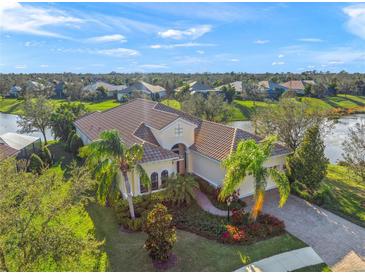 An impressive single-story home with a tile roof, lush landscaping, and picturesque lake views from an elevated perspective at 7108 Callander Cv, Lakewood Ranch, FL 34202