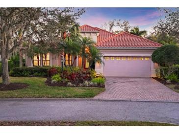 Charming single-story home with a red tile roof, lush landscaping, and a brick-paved driveway leading to an attached garage at 7665 Portstewart Dr, Lakewood Ranch, FL 34202