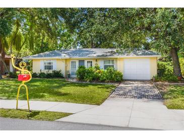 Charming yellow home featuring a well-manicured lawn, brick driveway, and lush landscaping at 1870 Jasmine Dr, Sarasota, FL 34239