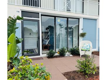 Inviting front entrance featuring tiled patio, sliding glass doors, and a cozy wicker chair surrounded by lush landscaping at 600 Manatee Ave # 114, Holmes Beach, FL 34217