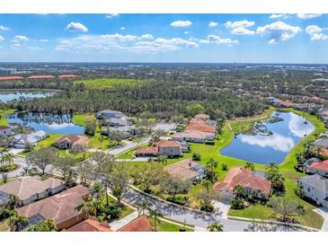 Aerial view of a beautiful neighborhood with tile-roofed homes, lush greenery, and sparkling lakes under a blue sky at 9612 Old Hyde Park Pl, Bradenton, FL 34202