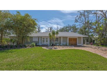 Well-maintained home exterior with a green lawn, beautiful trees, and brick driveway at 618 Buttonwood Dr, Longboat Key, FL 34228