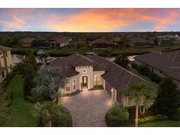 Stunning single-story waterfront home boasts a terracotta roof, brick driveway, and lush landscaping at sunset at 11739 River Shores Trl, Parrish, FL 34219