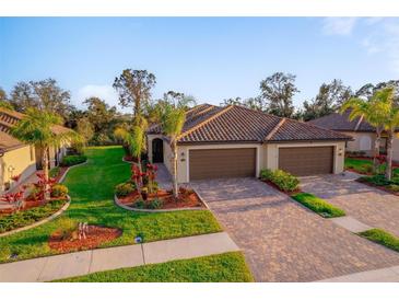 Charming home featuring a well-maintained lawn, mature palm trees, and a paver driveway leading to a three-car garage at 12151 Amica Loop, Venice, FL 34293