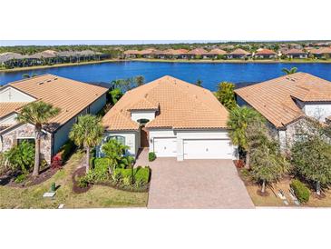 Waterfront home featuring a tile roof, brick driveway, a well-manicured yard, and an attached two car garage at 7036 Whittlebury Trl, Lakewood Ranch, FL 34202
