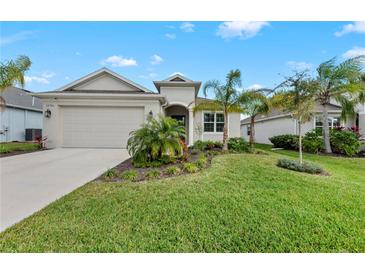 Inviting single-story home with a well-manicured lawn and lush landscaping, including palm trees and flowering plants at 12726 Rainwashed Loop, Parrish, FL 34219