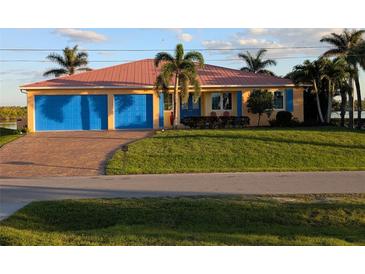 Charming home featuring a well-manicured lawn, a salmon-colored metal roof, and vibrant blue garage doors at 3572 Peace River Dr, Punta Gorda, FL 33983