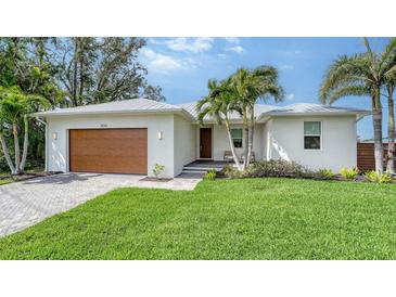 Charming single-story home with a well-manicured lawn, modern wood garage door, and lush tropical landscaping at 6136 Hollywood Blvd, Sarasota, FL 34231