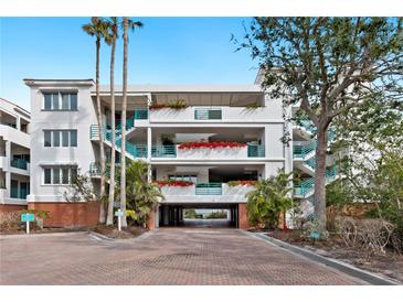 Condo building with balconies, lush landscaping, covered parking, and brick paver drive at 340 Gulf Of Mexico Dr # 115, Longboat Key, FL 34228