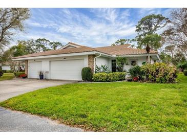 Charming home featuring a lush green lawn, beautiful landscaping, and a white exterior with a tiled roof at 5614 Garden Lakes Dr, Bradenton, FL 34203
