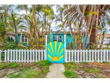 Charming home with a bright blue exterior, surrounded by lush palm trees, and featuring a whimsical gate at 256 144Th Ave, Madeira Beach, FL 33708