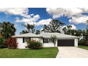 Charming single-story home featuring a well-manicured lawn, red hibiscus, and an attached two-car garage at 800 Everest Rd, Venice, FL 34293