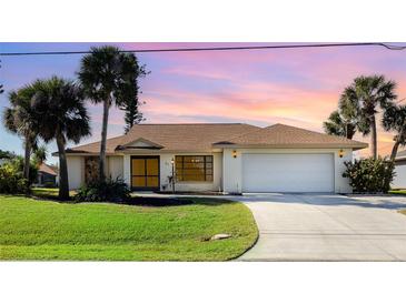 Charming single-story home with a manicured lawn, mature palm trees and a two-car garage with beautiful sunset sky backdrop at 31 Bunker Rd, Rotonda West, FL 33947