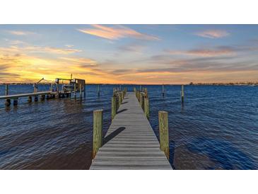 Long wooden dock extends into serene waters, featuring mooring posts, boat lift, and a picturesque sunset backdrop at 2512 Riverside E Dr, Bradenton, FL 34208