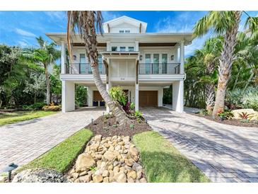 Stunning two-story coastal home featuring lush tropical landscaping and a brick paver driveway at 516 Kumquat Dr, Anna Maria, FL 34216