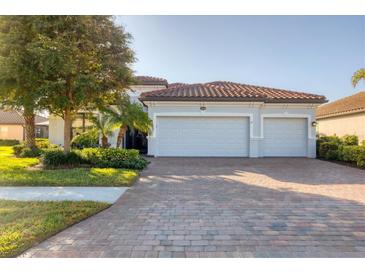 Charming home featuring a three-car garage, red tile roof, beautiful landscaping, and a brick paver driveway at 13145 Amerigo Ln, Venice, FL 34293