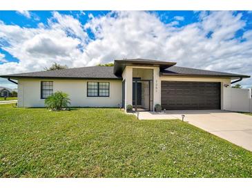 Well-maintained single-story home with a manicured lawn, dark garage door, and decorative plants at 7251 Sunnybrook Blvd, Englewood, FL 34224