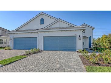 Exterior of a well lit two-story home with a light brick driveway and two-car blue garage doors at 2309 Blue Mahoe Ln, Sarasota, FL 34240