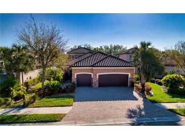 Charming home featuring a well-manicured lawn, mature landscaping, and a three-car garage with a tile roof at 9902 Craftsman Park Way, Palmetto, FL 34221