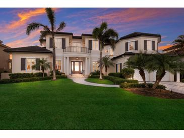 A luxurious two-story home featuring a well-manicured lawn, mature palms, and elegant architectural details at sunset at 348 W Royal Flamingo Dr, Sarasota, FL 34236