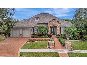 Stunning single-story home features a stone-accented entry, lush landscaping, and a brick-paved driveway leading to a two-car garage at 3843 E 59 Avenue Cir, Ellenton, FL 34222