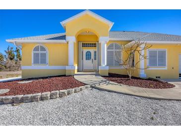 Inviting yellow home featuring a well-manicured landscape, stone accents, and a charming arched entryway at 240 Spaniards Rd, Placida, FL 33946