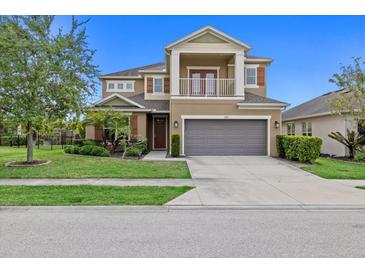 Two-story tan home with a two-car garage, front porch, second story balcony, and manicured lawn at 5954 Anise Dr, Sarasota, FL 34238