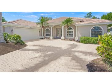 Charming home featuring a tiled roof, arched windows, columns, palm trees, and a paver driveway at 5354 Nathaniel Pl, Sarasota, FL 34233