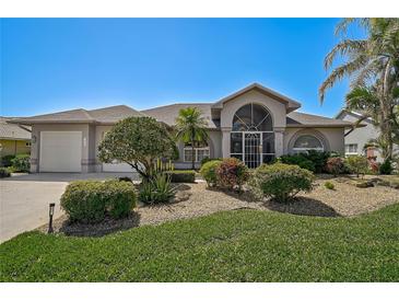 Charming single-story home featuring a well-manicured lawn, tropical plants and a covered entryway with decorative accents at 457 Lake Of The Woods Dr, Venice, FL 34293