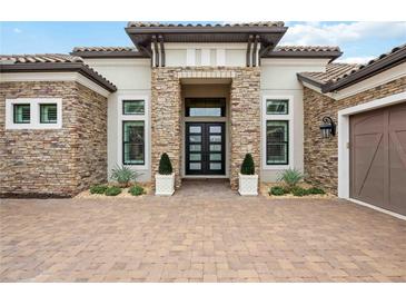 Close-up view of home showcasing stone accents, a tile roof, brick driveway, and manicured landscaping that create curb appeal at 5313 Greenbrook Dr, Sarasota, FL 34238