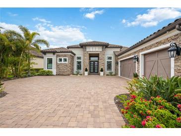 Stunning home featuring stone accents, a tile roof, brick driveway, and lush landscaping creating an inviting curb appeal at 5313 Greenbrook Dr, Sarasota, FL 34238
