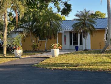 Charming yellow home featuring a metal roof, tropical landscaping, and a welcoming front entrance at 7036 Clark Rd, Sarasota, FL 34241