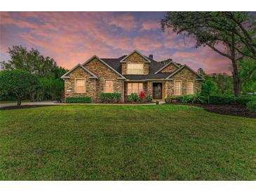 Beautiful stone home featuring a manicured lawn and colorful landscaping at 22235 Panther Loop, Bradenton, FL 34202