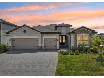 Beautiful exterior elevation with a three-car garage, paver driveway, stone accents and lush landscaping at 15104 Blue Bay Ter, Lakewood Ranch, FL 34211