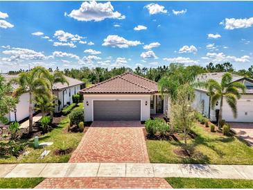 Beautiful home with a red brick driveway and tropical landscaping, including palm trees and lush green grass at 17714 Northwood Pl, Bradenton, FL 34202