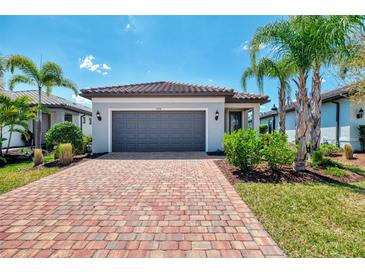 Charming home featuring a red brick driveway, gray garage door, and manicured landscaping with lush bushes at 17714 Northwood Pl, Bradenton, FL 34202