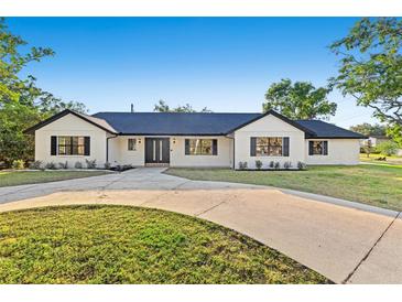 Charming one-story home boasts a white brick facade, black trim, and a spacious circular driveway at 1406 N Riverhills Dr, Temple Terrace, FL 33617